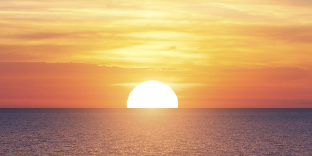 An image of the sun setting over the ocean. The sky is bright orange.