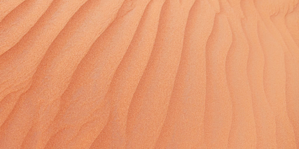 Panoramic view of desert sand in fine grain, marked with soft regular ripples.